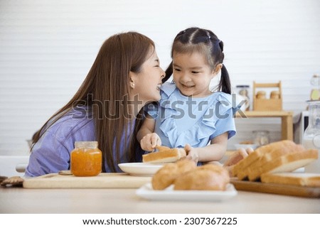 kid putting orange jam on bread toast with her mother in the kitchen