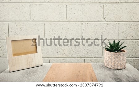 Concept shot of blank wooden photo frame on gray wooden table with green plant in the pot with brick wall background 