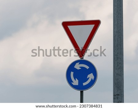 Close-up photo of a yield and roundabout traffic sign attached to a metal post next to an electric pole