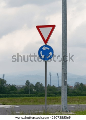 Close-up photo of a yield and roundabout traffic sign attached to a metal post next to an electric pole