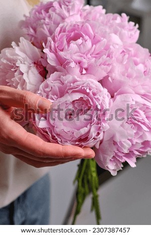 Happy woman holding pink peonies in her hands. The florist girl collected a bouquet of peonies. Delicate flowers are beautiful. A gift for the holiday, spring mood. Romantic surprise