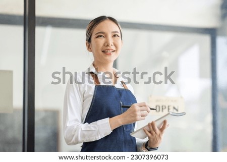Asian Happy business woman is a waitress in an apron, the owner of the cafe stands at the door with a sign Open waiting for customers , cafes and restaurants Small business concept.
