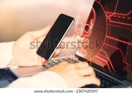 Close up of male hands using laptop and cellphone with digital skull hologram on blurry background. Hacking, malware and crime concept. Double exposure
