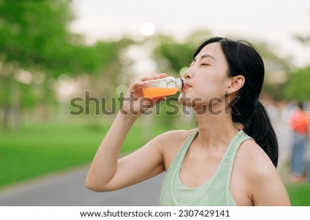Female jogger. Fit Asian young woman with green sportswear drinking organic orange juice after running and enjoying a healthy outdoor. Fitness runner girl in public park. Wellness being concept Royalty-Free Stock Photo #2307429141