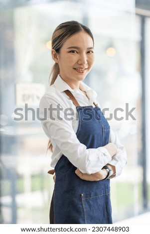 Asian Happy business woman is a waitress in an apron, the owner of the cafe stands at the door with a sign Open waiting for customers , cafes and restaurants Small business concept.

