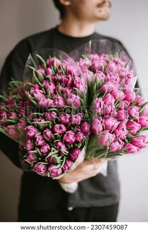 Young man holding a huge bunch of blossoming purple tulips, close up vertical image 