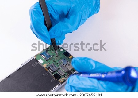 Close-up of the hands of a person with blue gloves who is repairing a mobile phone on a white background