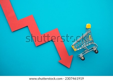 Shopping trolley with red chart falling down on blue background copy space. Global economic recession crisis, core retail sales decrease, inflation or goods price up concept. Royalty-Free Stock Photo #2307461919