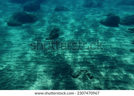 Underwater deep seascape with pattern on the sandy seabed. Rocks and sand in the ocean. Sandy bottom with stones, underwater picture from scuba diving. Adventure trip in the ocean, travel photo.