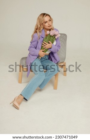 A young beautiful blonde woman with a bouquet of flowers is sitting on a chair