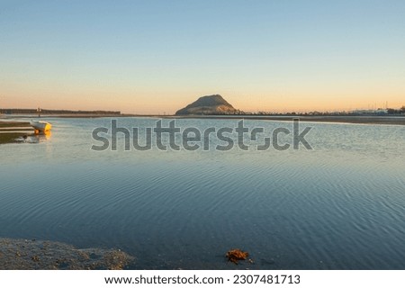 Landmark Mount Maunganui on distant horizon at sunrise with old-fashioned clinker dinghy on beach at Harbour Drive Tauranga.
