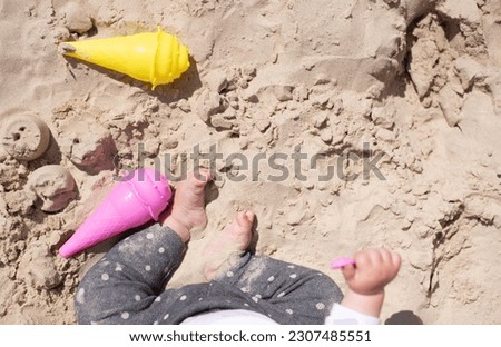 Little cute legs feet of child and  pink and yellow molds of ice cream for sand. Summer time baby joy and play in sand outdoor. Great vacation with children.