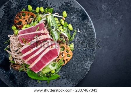 Modern style traditional Japanese gourmet seared tuna fish steak tataki with soba noodles and stir-fried vegetables served as top view on a Nordic design plate with copy space right Royalty-Free Stock Photo #2307487343