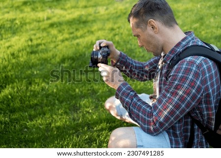 Side view of male photographer with photo camera outdoor. photo session on a summer vacation on the background of green grass. 