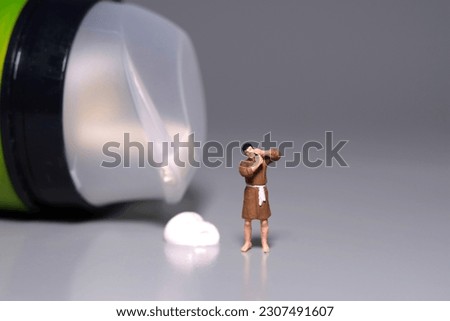 Miniature tiny people toy figure photography. A man getting shaving his beard standing beside shaving soap and cream on grey background. Image photo