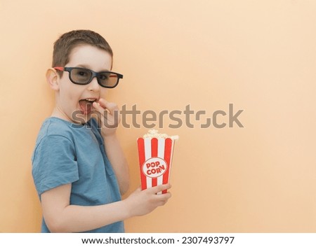 Caucasian boy in black 3d glasses holds popcorn on a beige background, copy space
