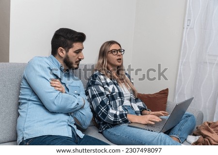 Young happy lovely couple planning budget together at home, writing notes to laptop computer, creating checklist for shopping or guest list for wedding invitations, counting chairs on ceremony