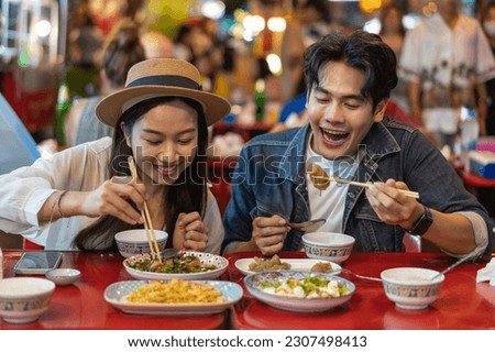 Young Asian couple traveler tourists eating Thai street food together in China town night market in Bangkok in Thailand - people traveling enjoying food culture concept Royalty-Free Stock Photo #2307498413