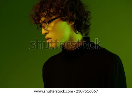 Young male portrait close-up in glasses fashion and style, hipster lifestyle, portrait green background mixed neon light, copy space