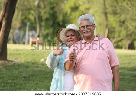 Indian happy senior couple showing thumb in garden and looking in front of camera Royalty-Free Stock Photo #2307516885