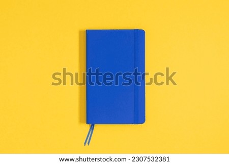 Flat lay, top view on blue closed  notepad on elastic band isolated on yellow background