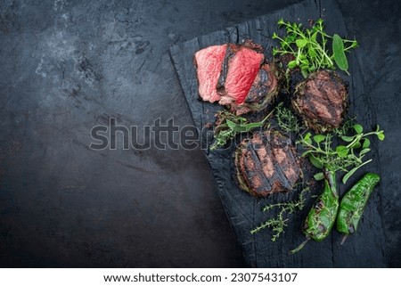 Traditional barbecue dry aged angus medaillon beef filet steak natural with herbs and red wine salt served as top view on a charred wooden board with copy space left  Royalty-Free Stock Photo #2307543107