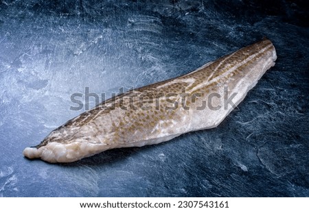 Raw Norwegian skrei cod fish filet with skin offered as close-up on black board with copy space 