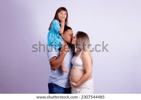 Pregnant loving couple giving a kiss and expressive daughter playing