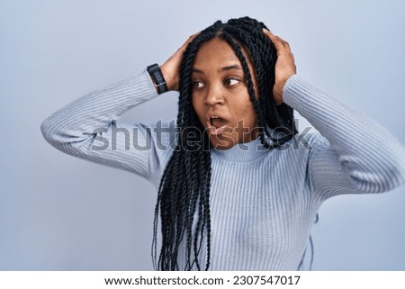 African american woman standing over blue background crazy and scared with hands on head, afraid and surprised of shock with open mouth 
