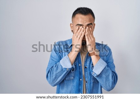 Young hispanic man standing over isolated background rubbing eyes for fatigue and headache, sleepy and tired expression. vision problem 