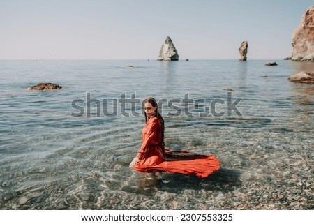 Woman travel sea. Happy tourist in red dress enjoy taking picture outdoors for memories. Woman traveler posing in sea beach, surrounded by volcanic mountains, sharing travel adventure journey