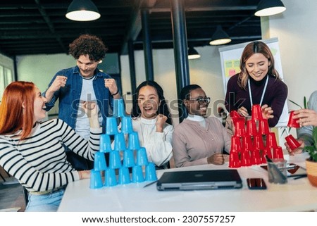 Group of young businesspeople playing, building towers from plastic cups, two teams, blue and red. Teambuilding activity. Royalty-Free Stock Photo #2307557257