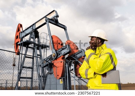 Oil rig worker in protective equipment observing production of crude oil in the field. Royalty-Free Stock Photo #2307567221