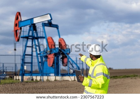 Industrial worker in protective work wear and hard hat monitoring drilling operations of oil rigs.