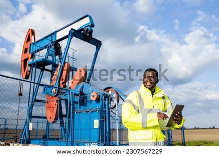 Oil filed supervisor with tablet computer standing by the pump jack and checking crude oil production.