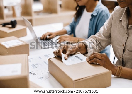 Unrecognizable online store owner sticking a barcode label onto a package box. Businesswoman preparing an order for shipping in a warehouse. Female entrepreneurs running an e-commerce small business. Royalty-Free Stock Photo #2307571631