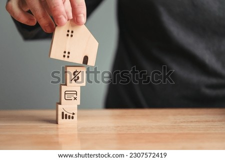 Man putting wooden house model on unstable factors for to apply for home loan. Fail and instability in housing loan. Real estate and business financial concept. Foundation economy house buying Royalty-Free Stock Photo #2307572419