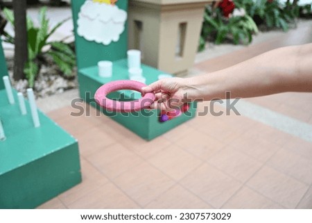 Hand holding a red rubber ring for throwing rings in throwing rings where players can throw green and blue rings into a white stick. Players help each other to throw as many rubber rings down the pole Royalty-Free Stock Photo #2307573029