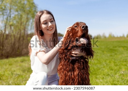 young girl petting brown dog breed Irish setter outdoors in the park, woman walks with pet in the summer on the lawn Royalty-Free Stock Photo #2307596087