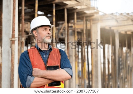 Senior smart engineering standing at construction site with scaffolding background, looking at contractors working on building houses and constructing utility infrastructure in real estate project  Royalty-Free Stock Photo #2307597307
