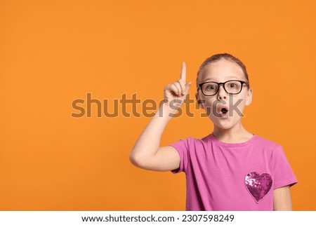 Portrait of cute girl in glasses on orange background. Space for text