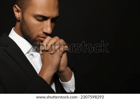African American man with clasped hands praying to God on black background. Space for text