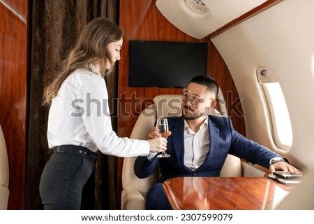 female stewardess serving glass of champagne to asian businessman in private luxury jet, korean financier manager in suit flying in plane and ordering champagne, luxury lifestyle