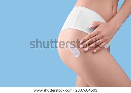Woman with smear of body cream on her leg against light blue background, closeup. Space for text