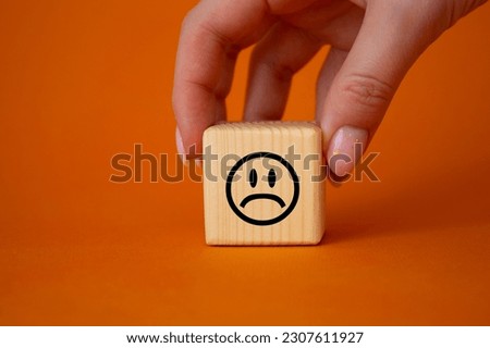 Sad smile symbol. Sad smile on wooden cube. Businessman hand. Beautiful orange background. Business and Sad smile concept. Copy space.