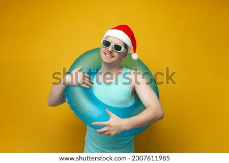 young guy in a New Year's hat in the summer on vacation with an inflatable swim ring rejoices and smiles, a man with a swim ring for Christmas