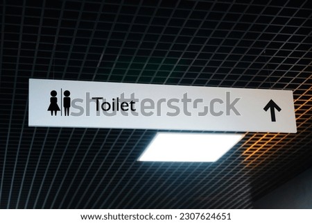 Hanging sign of public toilet with arrow showing direction
