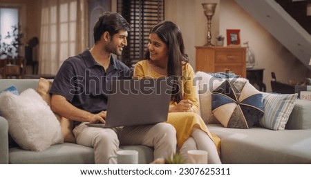 Portrait of Loving Young Indian Couple Enjoys Browsing Online Shopping Websites Together On A Laptop, While Sitting Cozily On Their Living Room Sofa. Browsing Interner, Choosing Products to Purchase Royalty-Free Stock Photo #2307625311