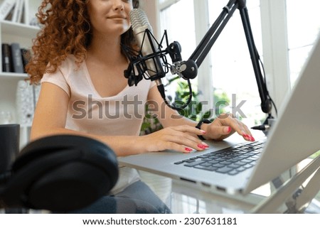 Woman vlogger looking at laptop and recording video with microphone