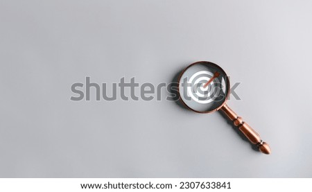 Magnifying glass to zoom in on dartboard goals and achievements in the business on gray background. Focused vision amplifying targets and Business Success concept.  Royalty-Free Stock Photo #2307633841